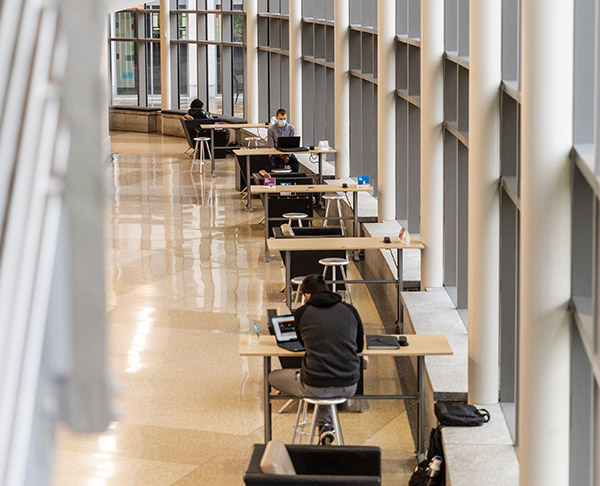 A hallway at the Indianapolis campus with desks along one side and an assortment of students sitting at them doing work. 